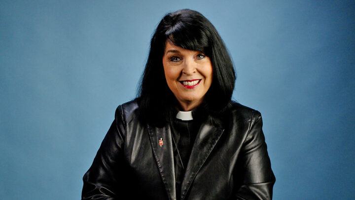 Bishop Connie Mitchell Shelton in a black leather jacket, sitting in front of a blue background