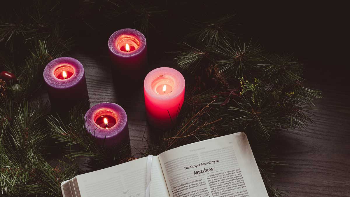 Advent wreath with candles lit next to a Bible opened to the book of Matthew