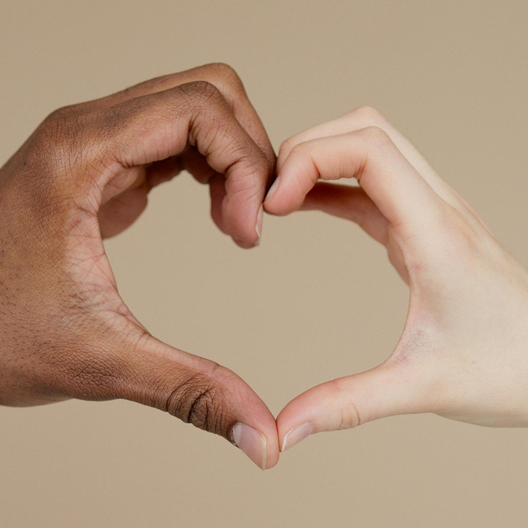 Two hands (one with darker skin than the other) making a heart shape